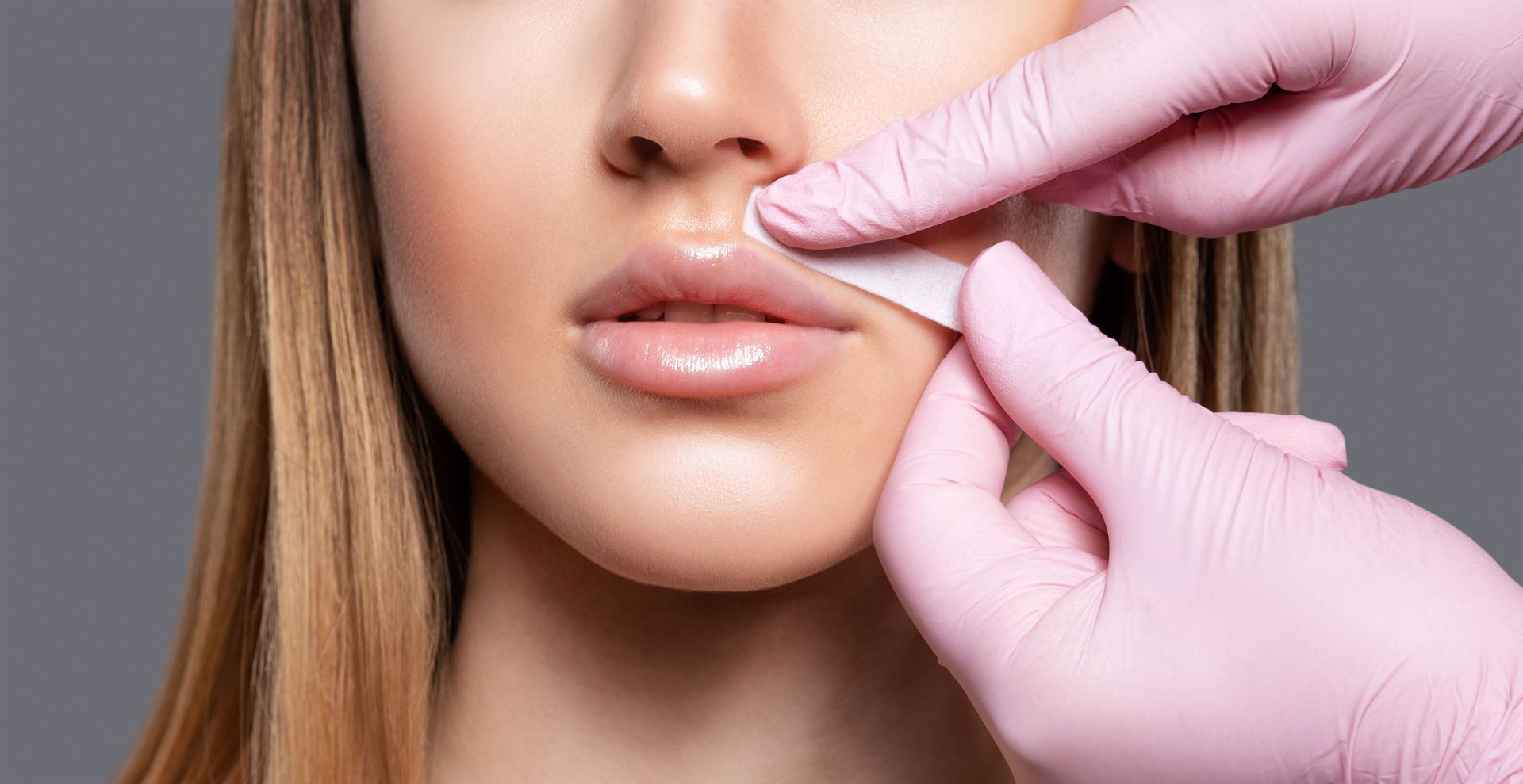 A woman is getting her lips waxed by a person wearing pink gloves.