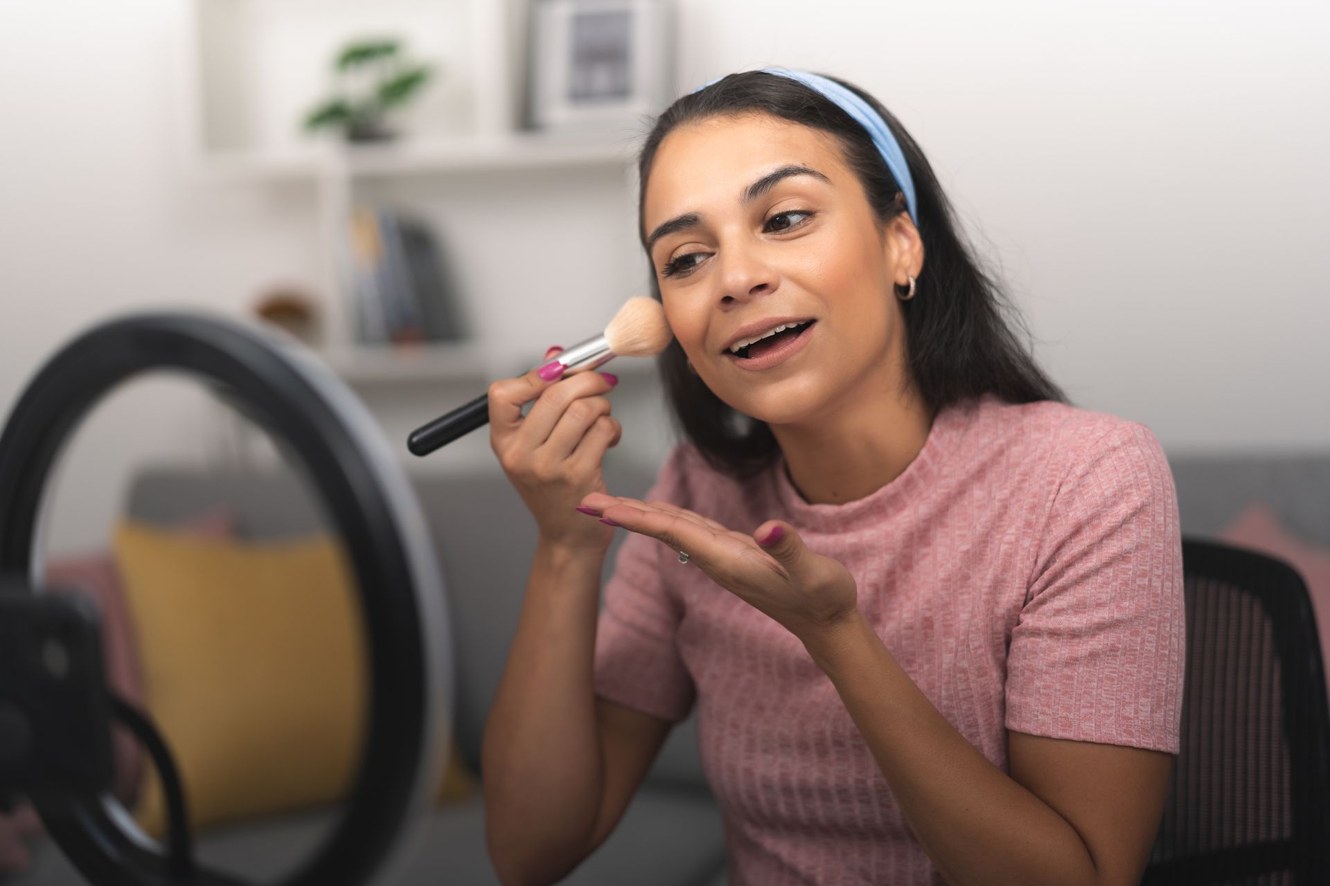 A woman is applying makeup in front of a ring light.