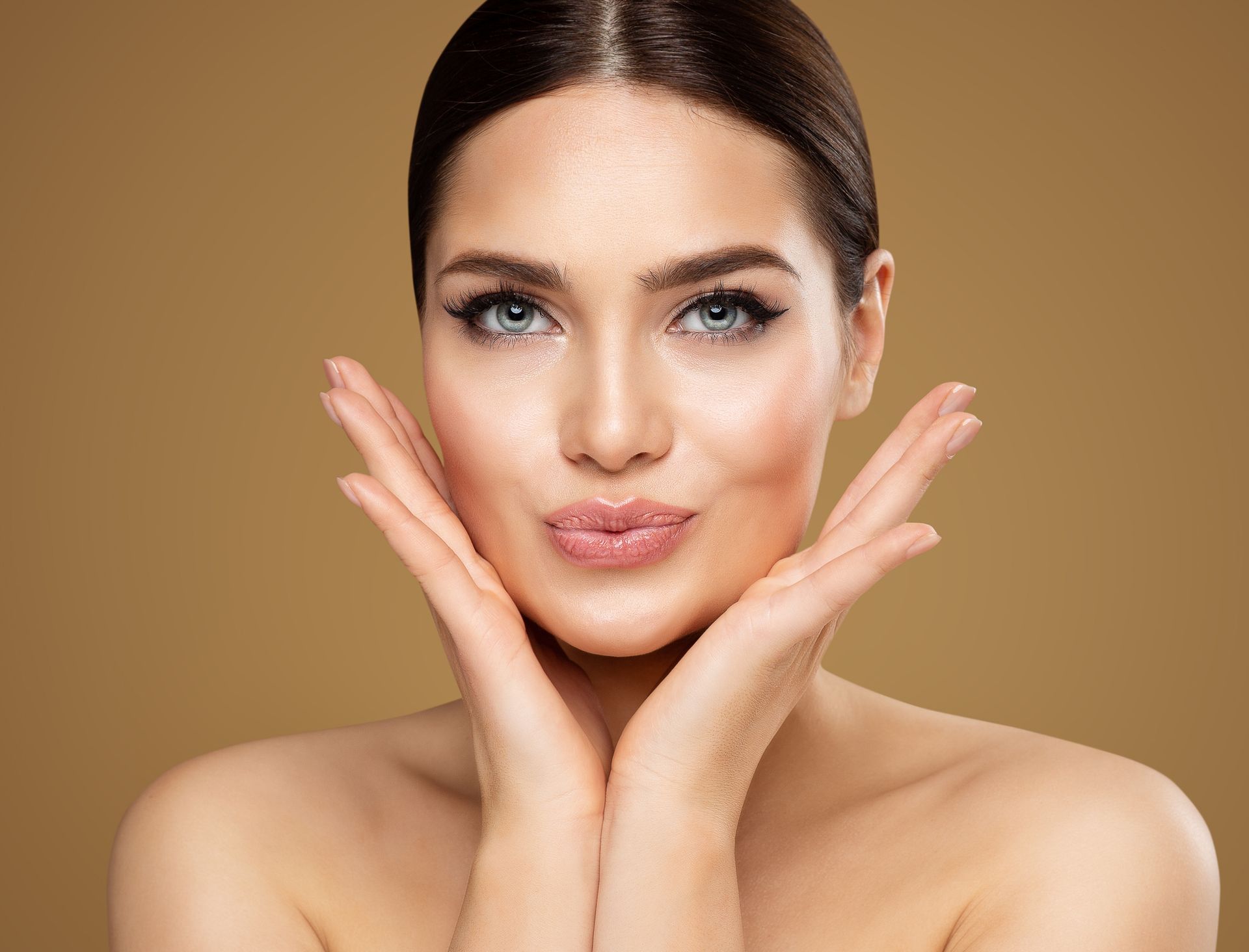 A woman is touching her face with her hands and smiling.