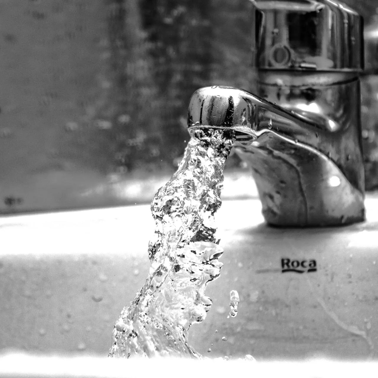 A black and white photo of water coming out of a roca faucet