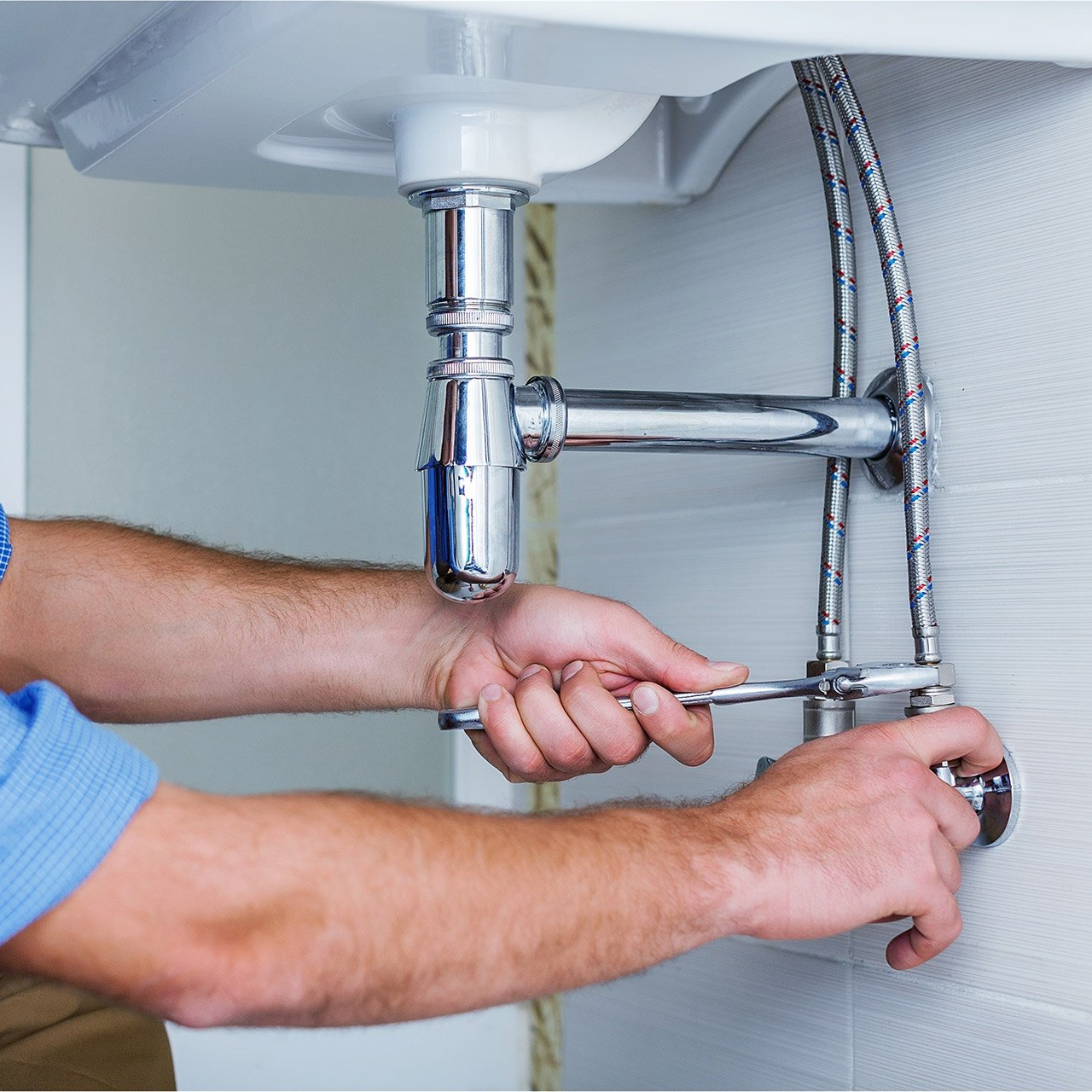 A man is fixing a sink with a wrench.