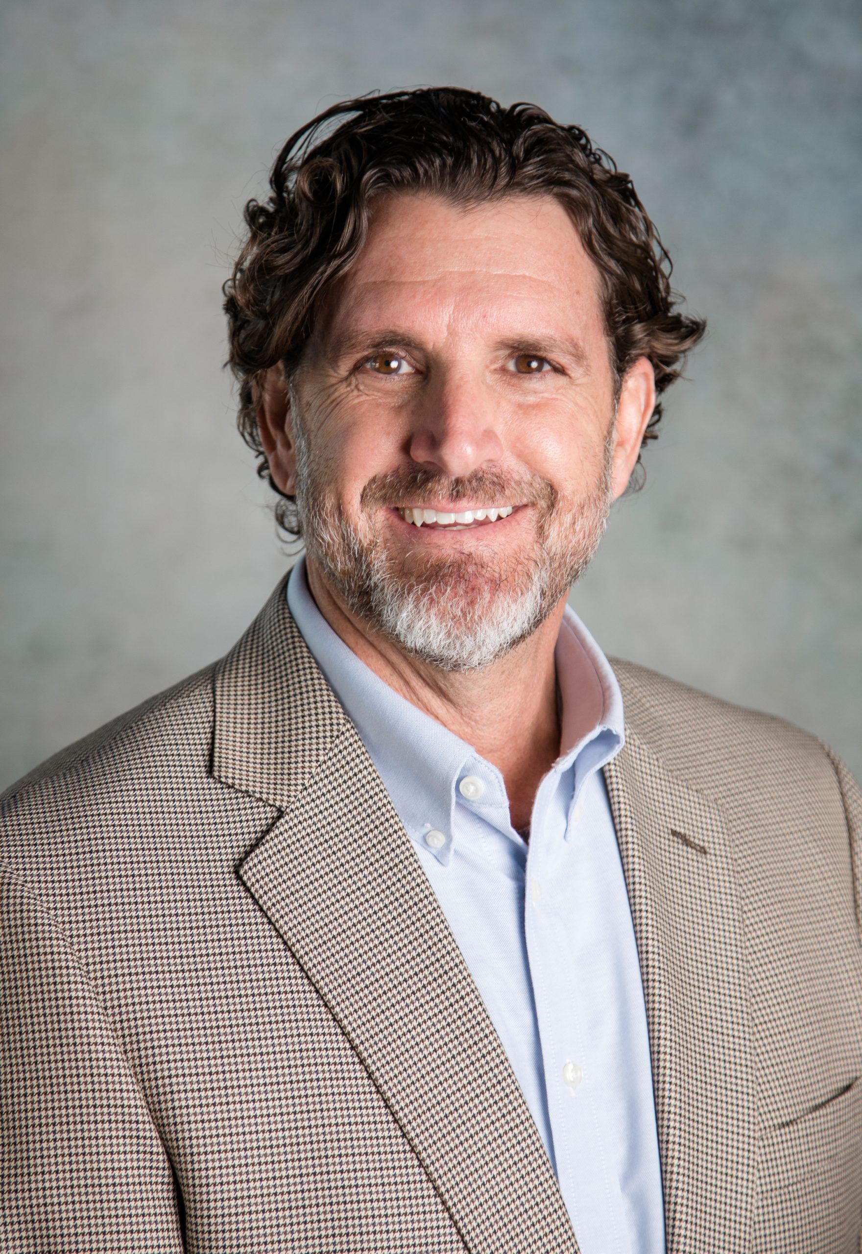 A man with a beard is wearing a suit and smiling for the camera.