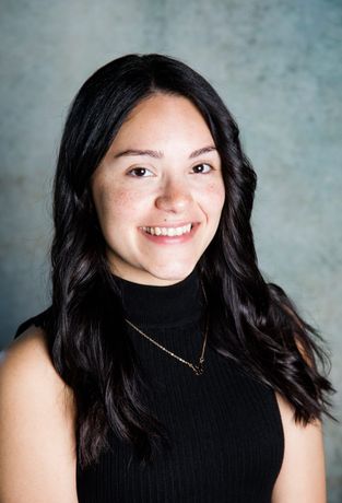A young woman wearing a black turtleneck and a necklace is smiling for the camera.