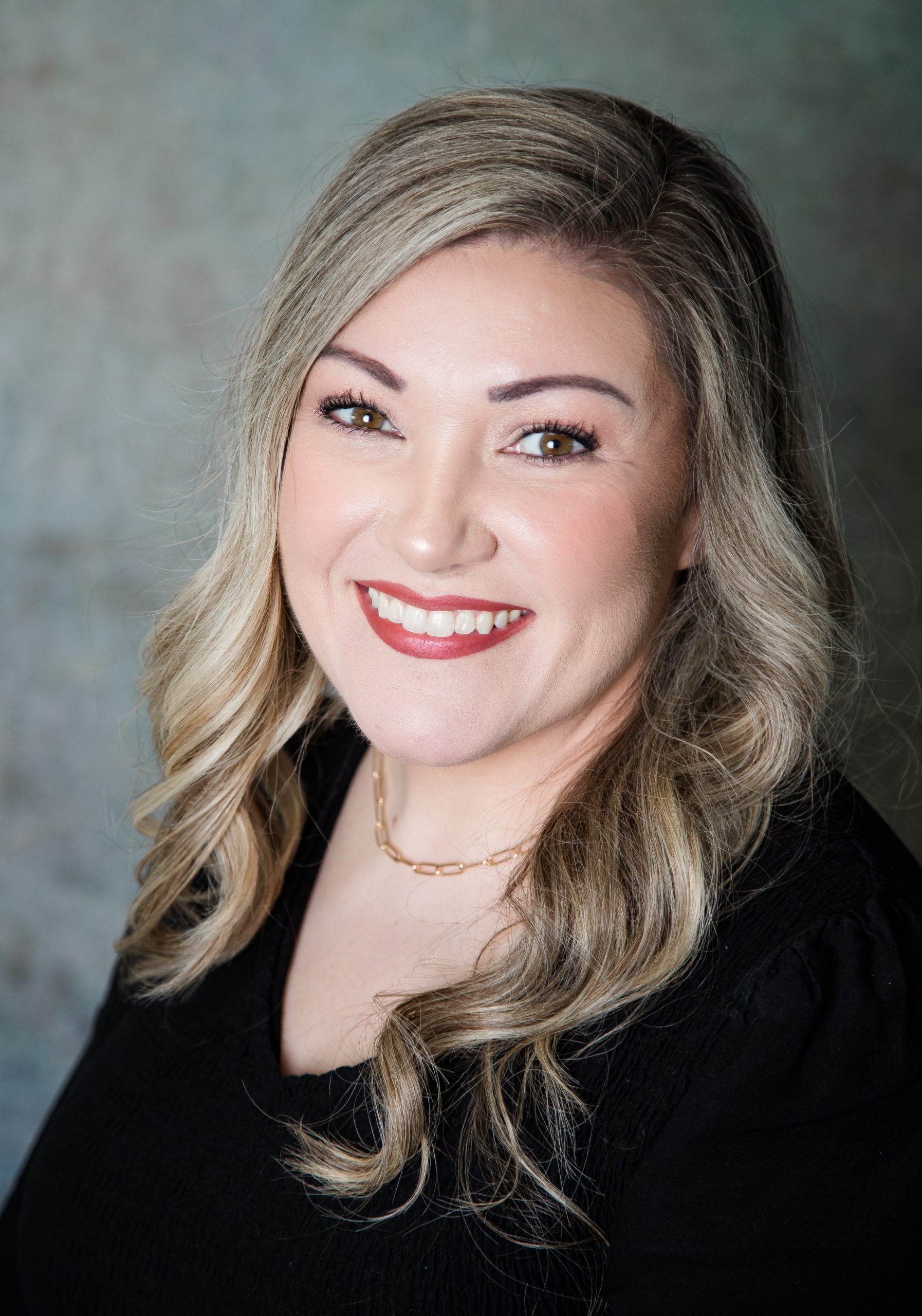 A woman wearing a necklace and a black shirt is smiling for the camera.