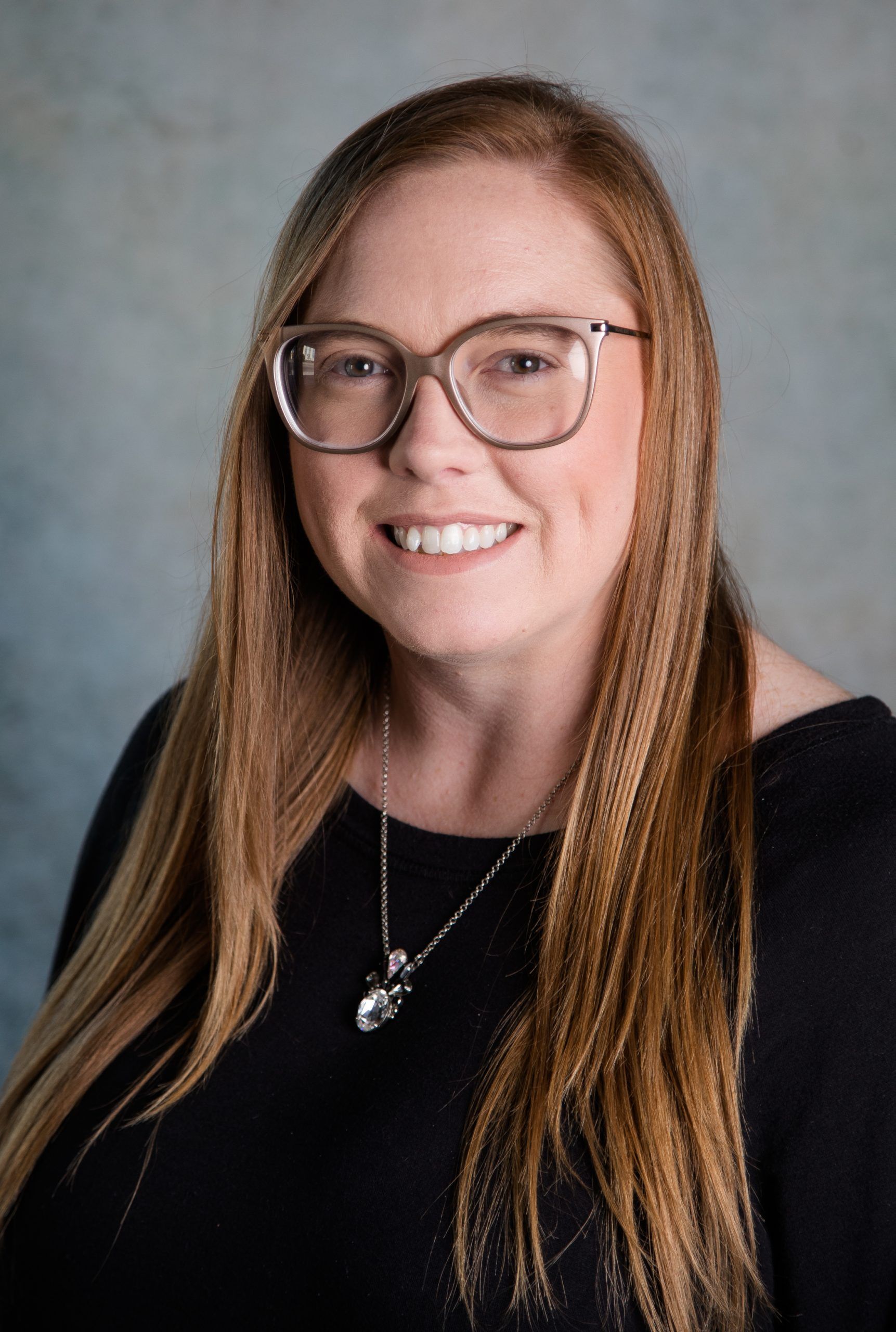 A woman wearing glasses and a necklace is smiling for the camera.