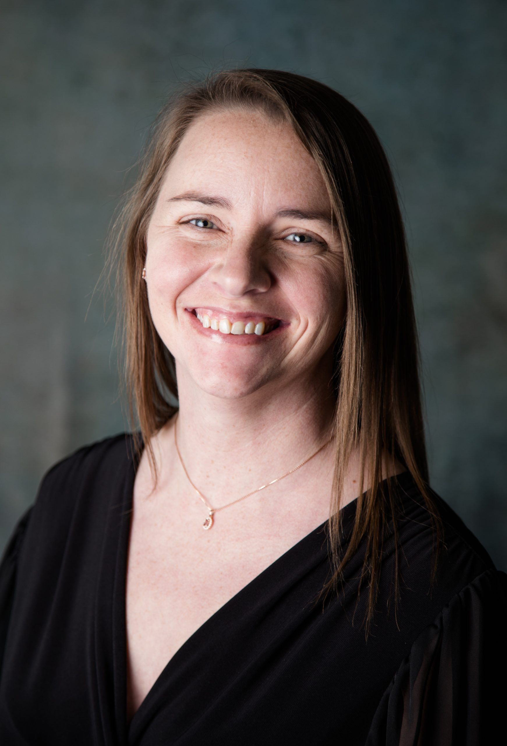 A woman wearing a black shirt and a necklace is smiling for the camera.