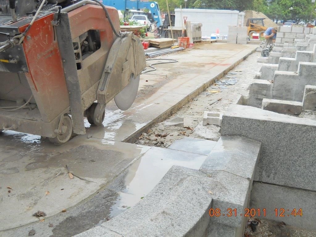 A concrete saw cutting through a concrete surface, with a construction site in the background.