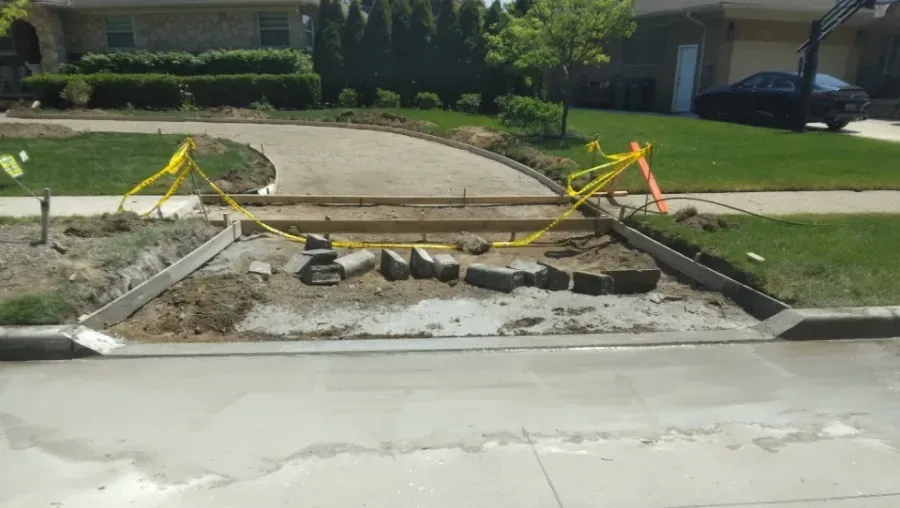 Driveway construction in progress, with caution tape, curb, concrete, and brick edging.
