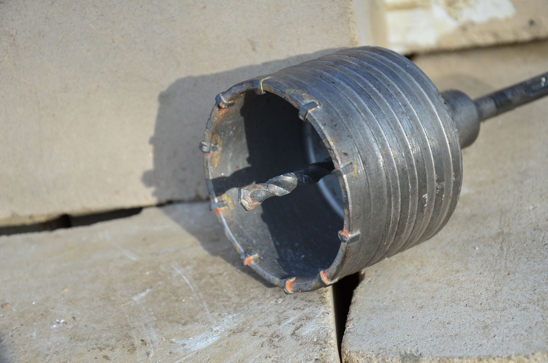 Hole saw drill bit on concrete block. Dark metal, round blade.