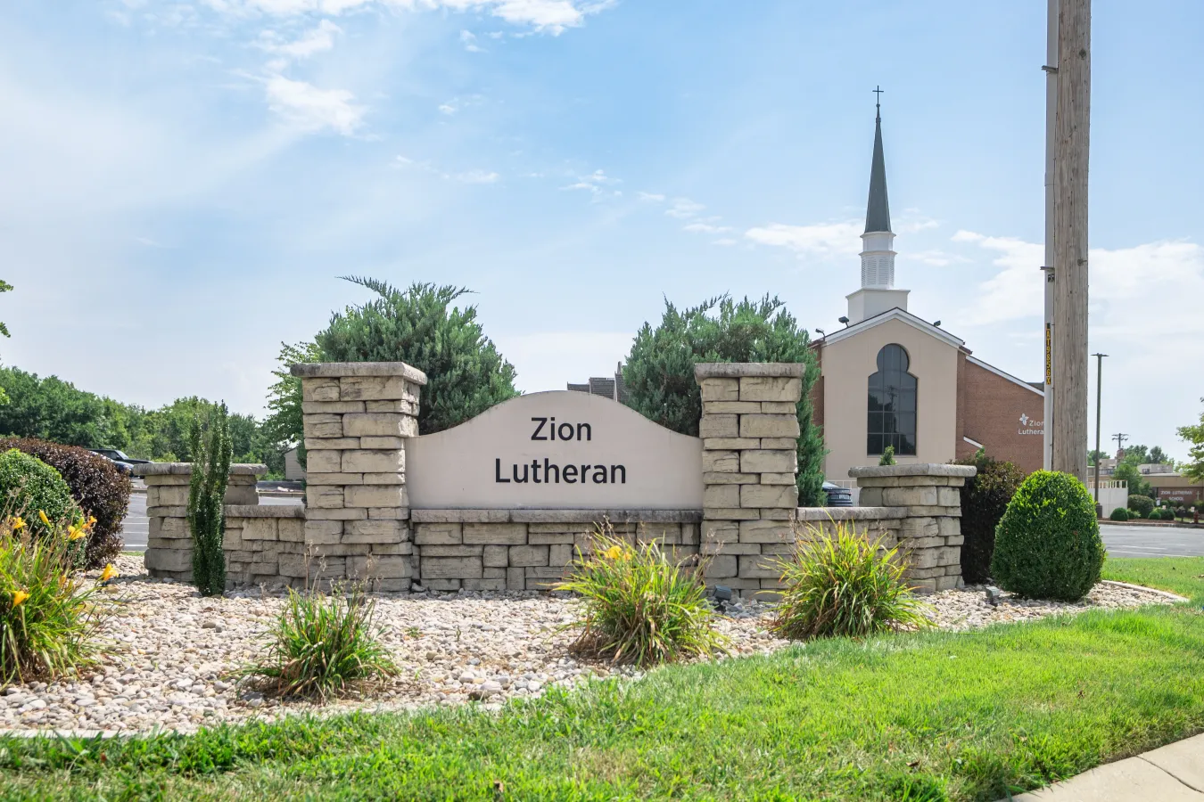 Sign for Zion Lutheran church with building and spire in background.