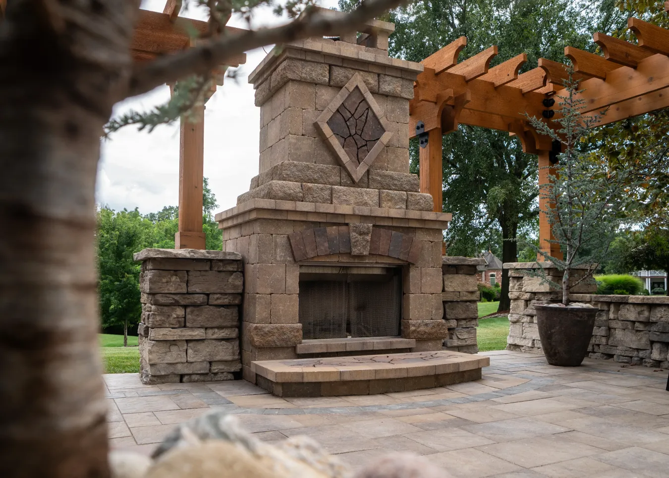 Stone outdoor fireplace with a diamond design, under a wooden pergola.