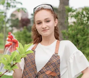 Woman in apron and safety glasses spraying a plant outdoors.