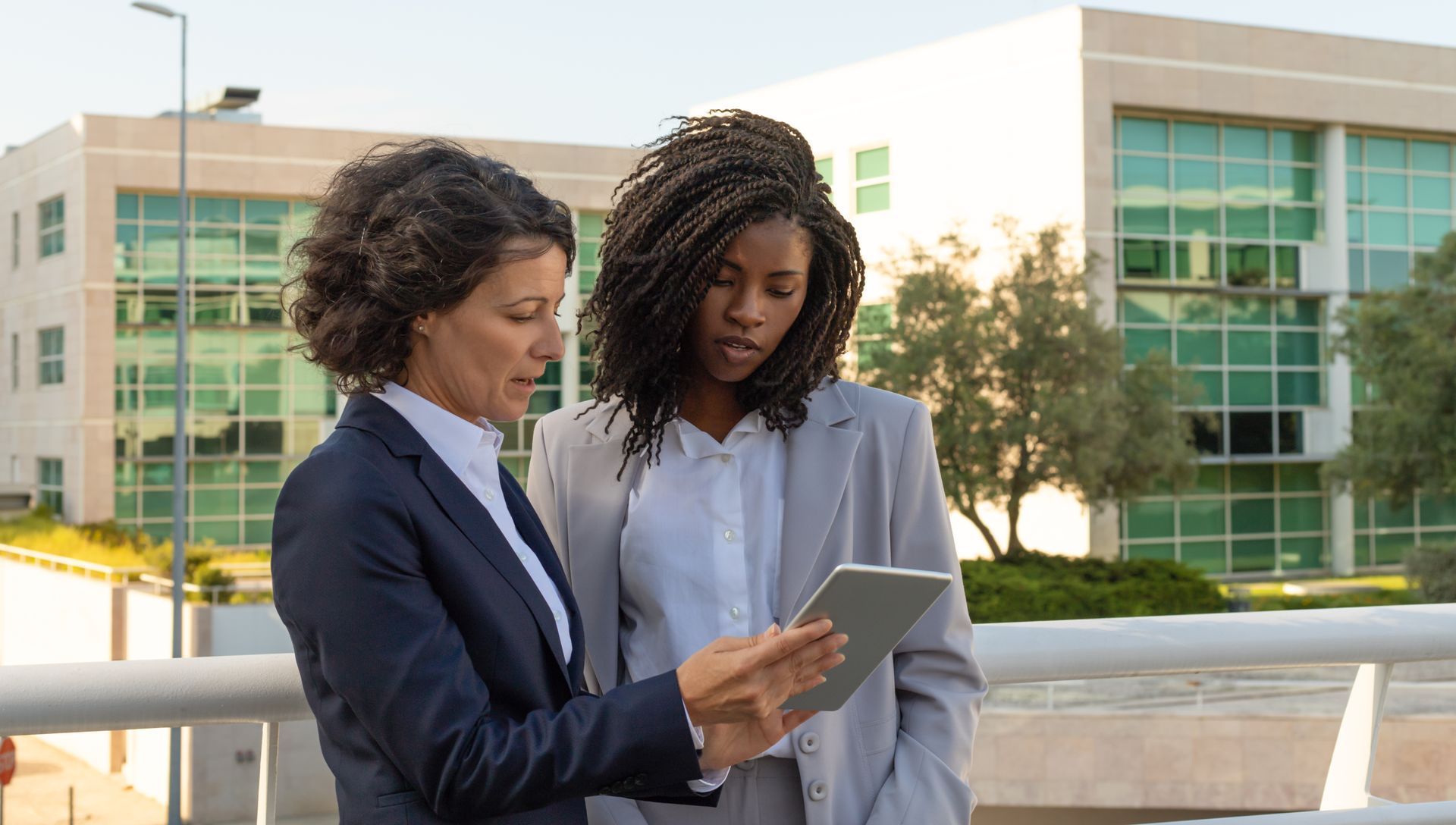 Two women are looking at a tablet together in front of a building.