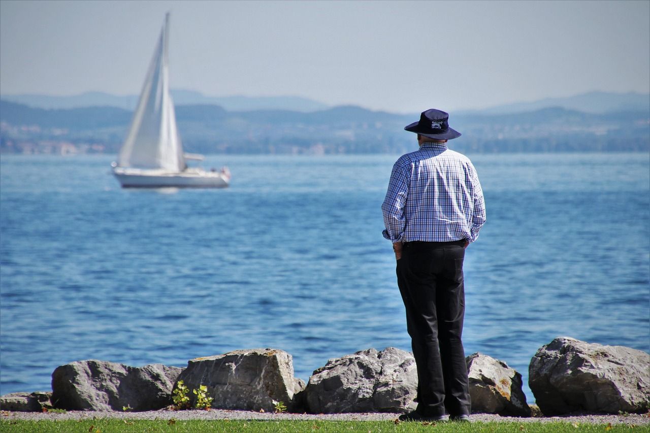 A man in a hat is looking at a sailboat in the water.