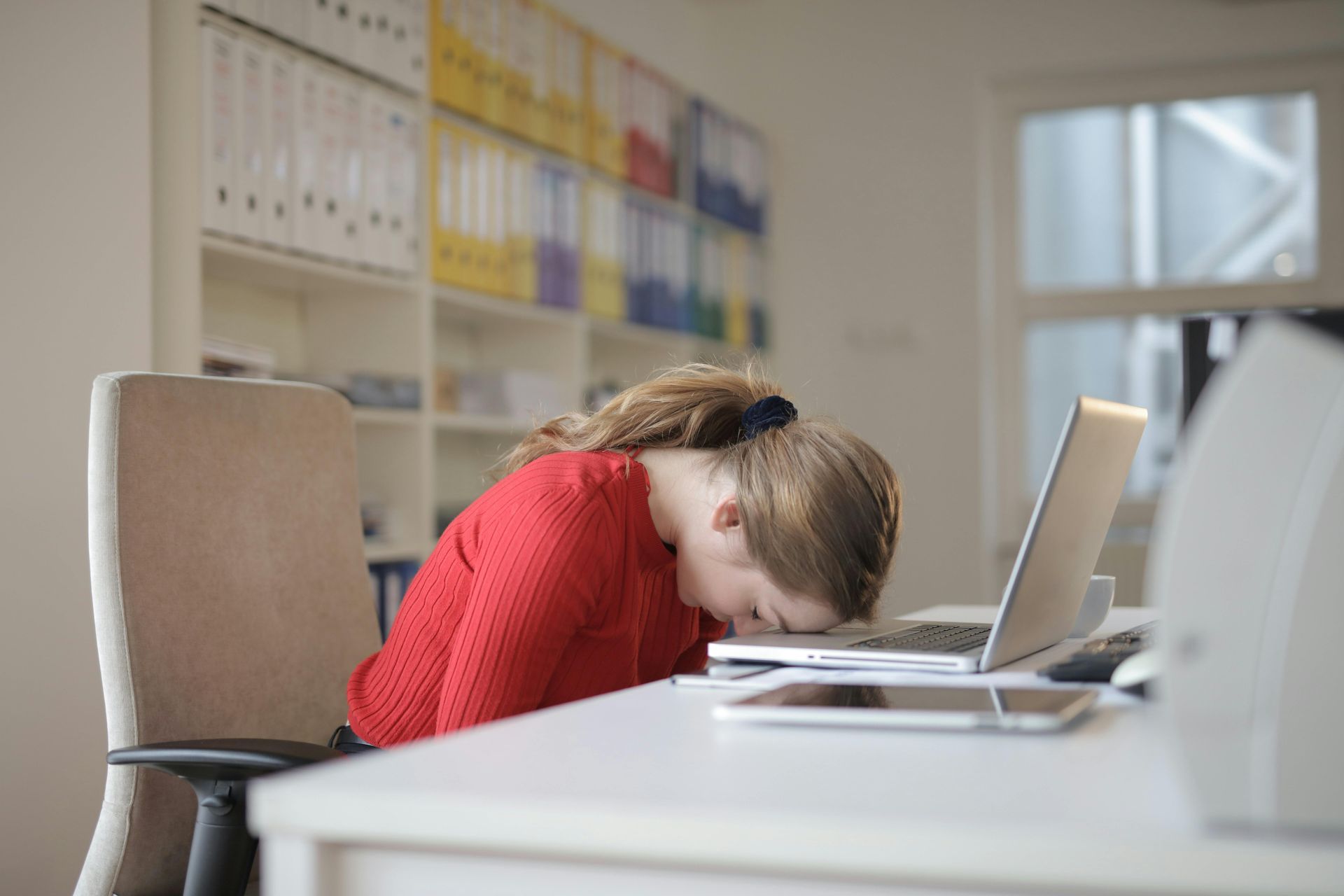 A woman is sitting at a desk with her head on a laptop computer.