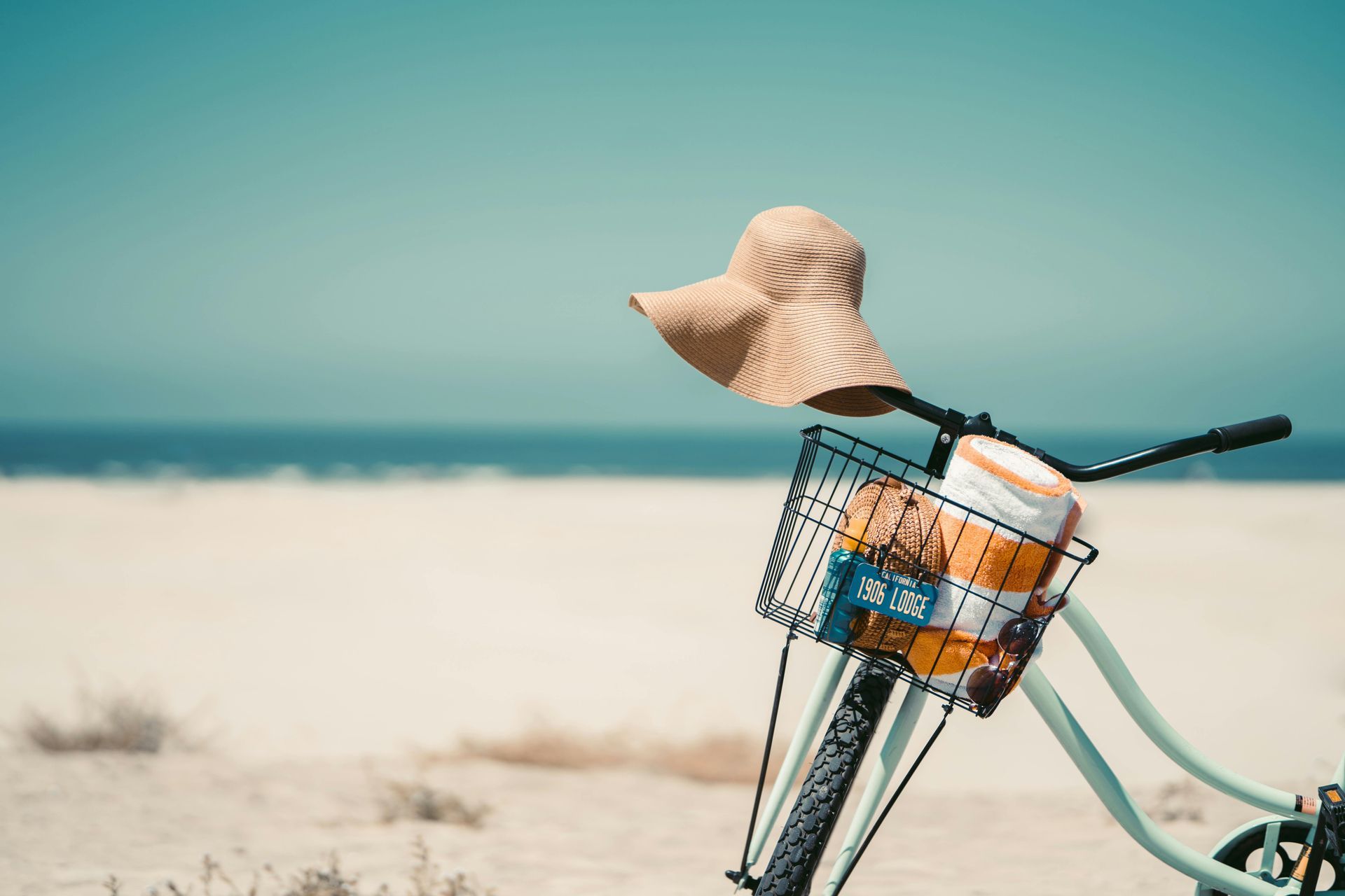 A bicycle with a basket and a hat on the beach.