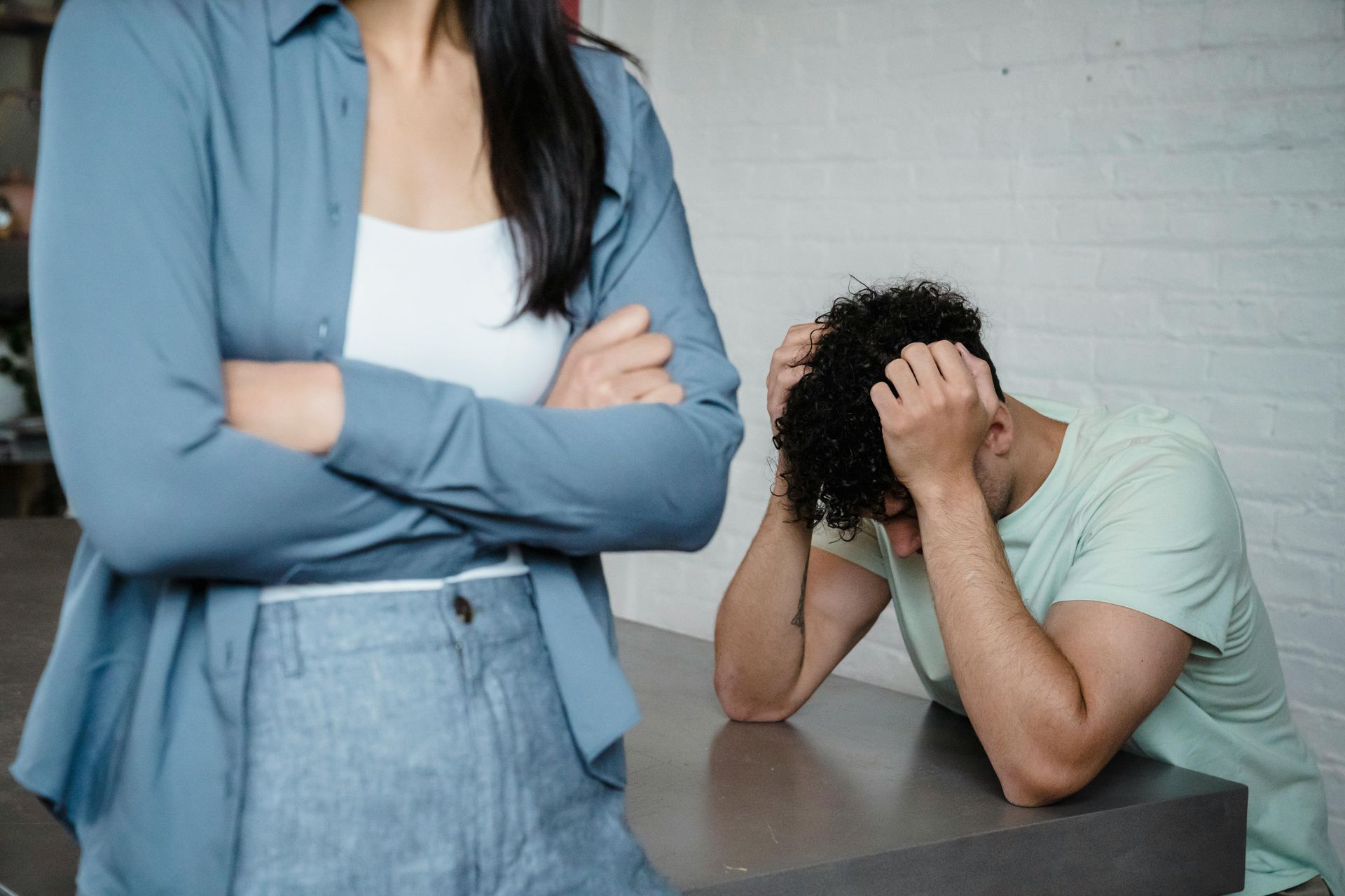 A woman is standing next to a man sitting at a table with his head in his hands.