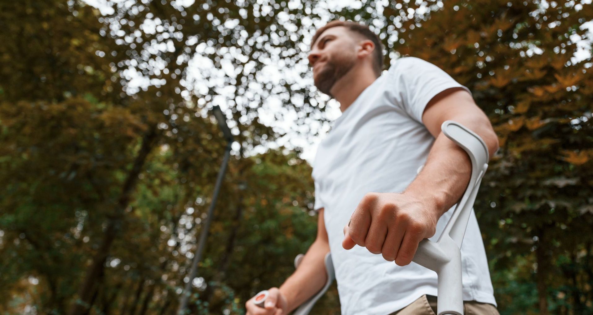 A man with a broken arm is walking with crutches in a park.