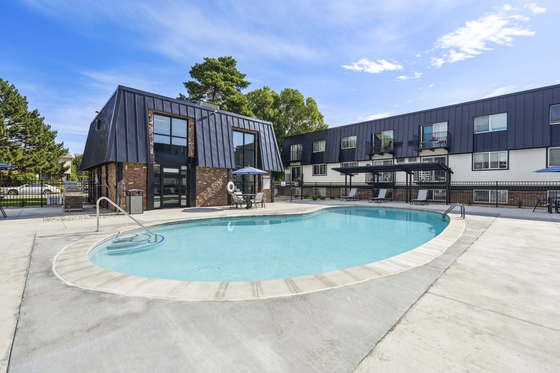 A kidney-shaped swimming pool in front of a multi-story hotel with black metal siding and a bright blue sky.