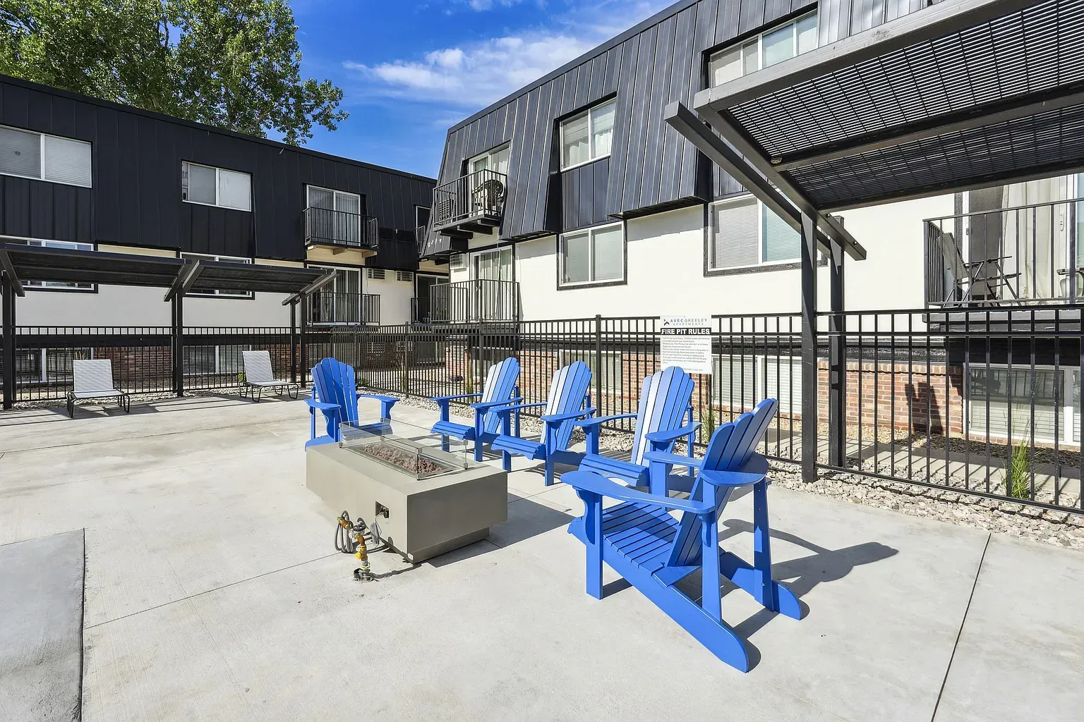 A modern outdoor patio featuring a central fire pit surrounded by several bright blue Adirondack chairs.