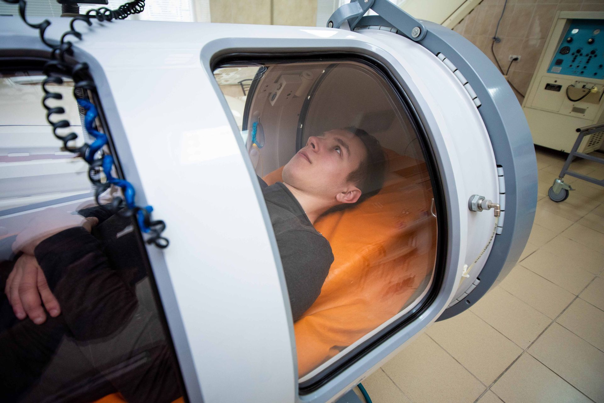 Patient lying in a hyperbaric oxygen chamber with an orange cushion and medical equipment nearby