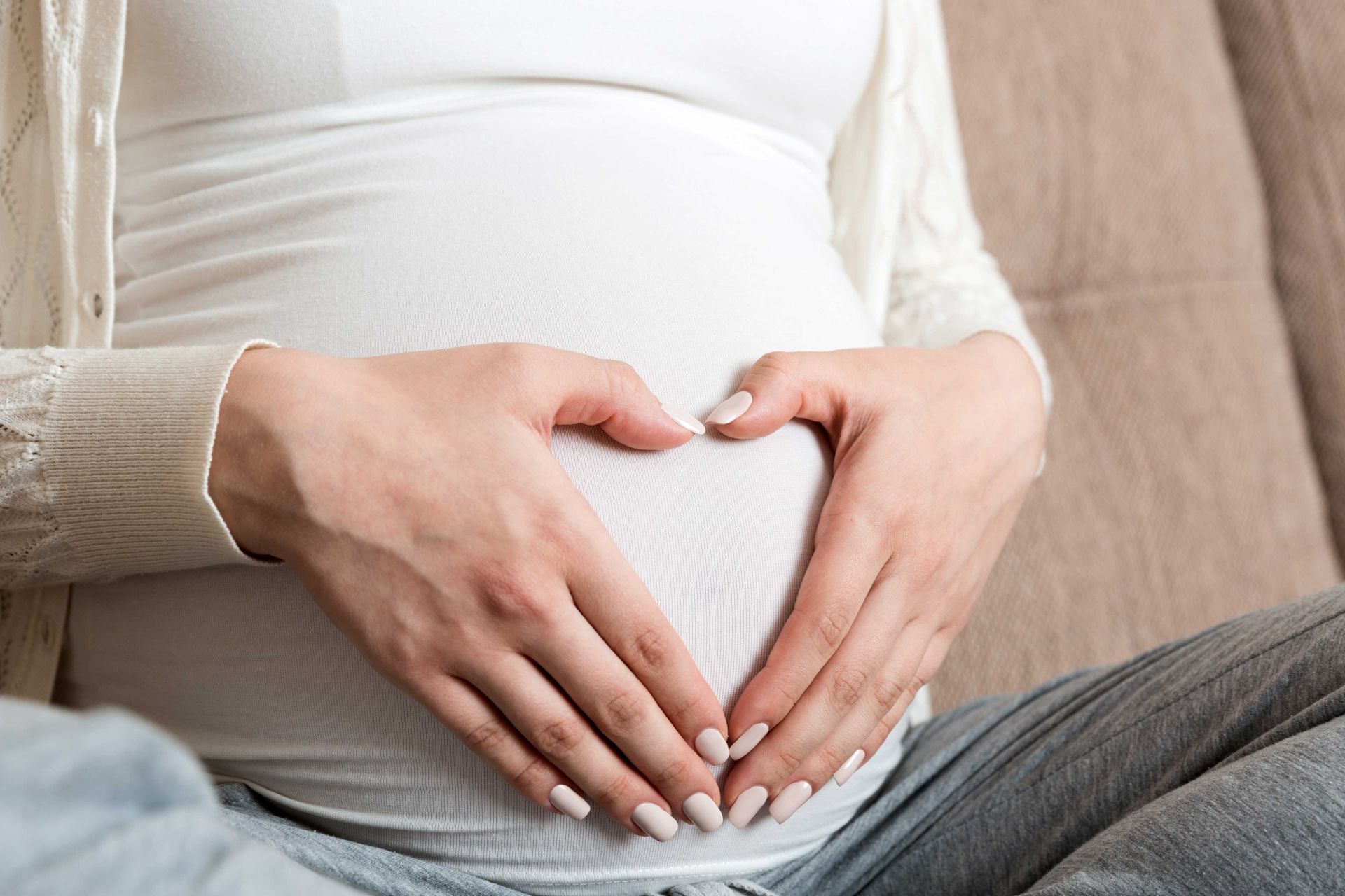 Hands forming a heart shape over a pregnant belly in a white shirt Hands forming a heart shape over a pregnant belly in a white shirt