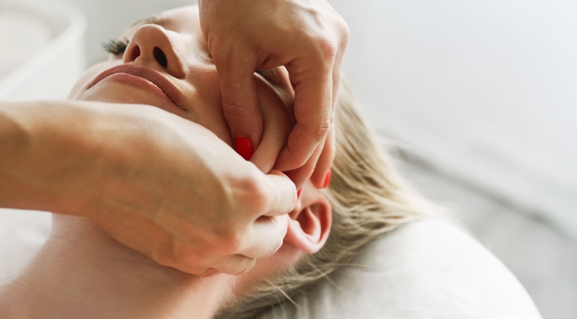 Hands pulling an ear to insert a red earring on a person lying on a pillow