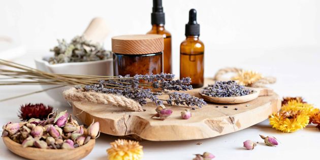 Herbal oils, dried flowers, and lavender arranged on a rustic wooden board with amber bottles
