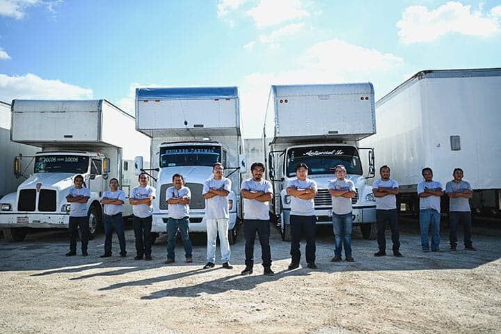 Un grupo de hombres está parado frente a una fila de camiones en movimiento.