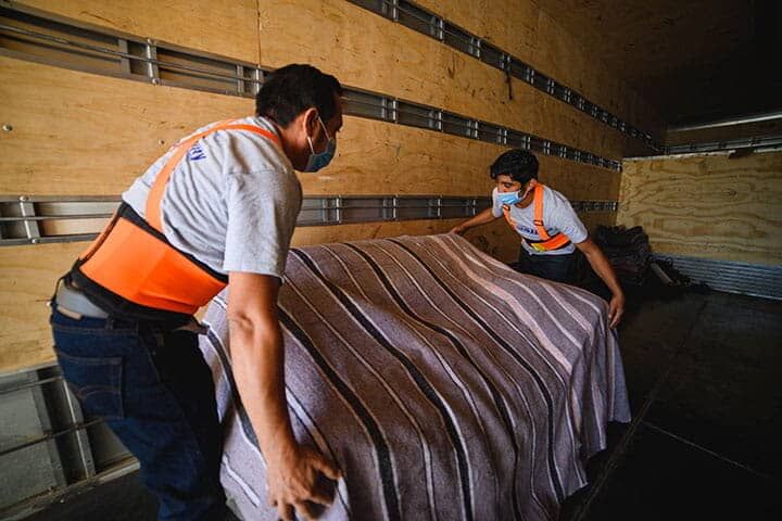 Dos hombres con máscaras mueven una cama en un camión.