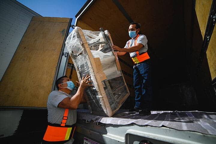 Dos hombres con máscaras cargan una máquina en un camión.