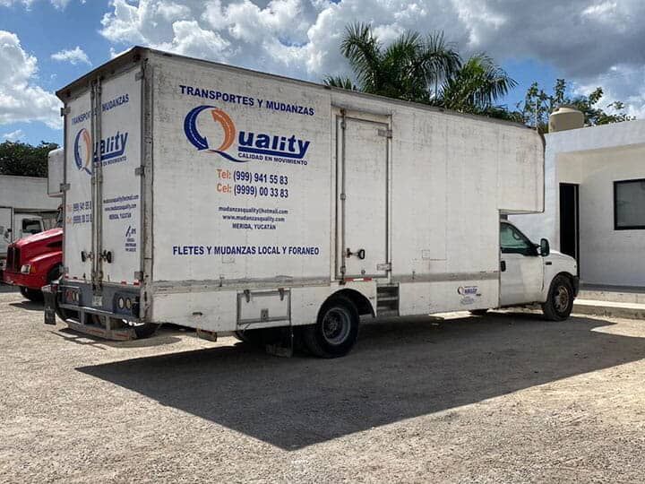 Una camioneta blanca con la palabra calidad en el costado está estacionada en un estacionamiento.