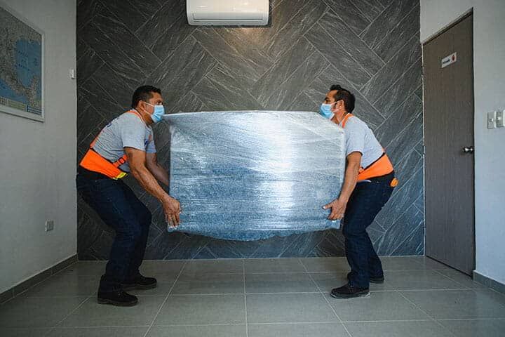 Dos hombres con máscaras llevan un gran trozo de metal en una habitación.