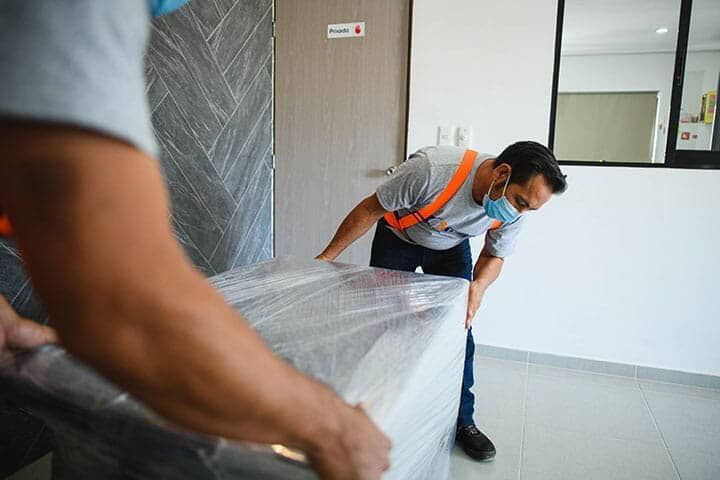 Un hombre con máscara levanta un colchón en una habitación.