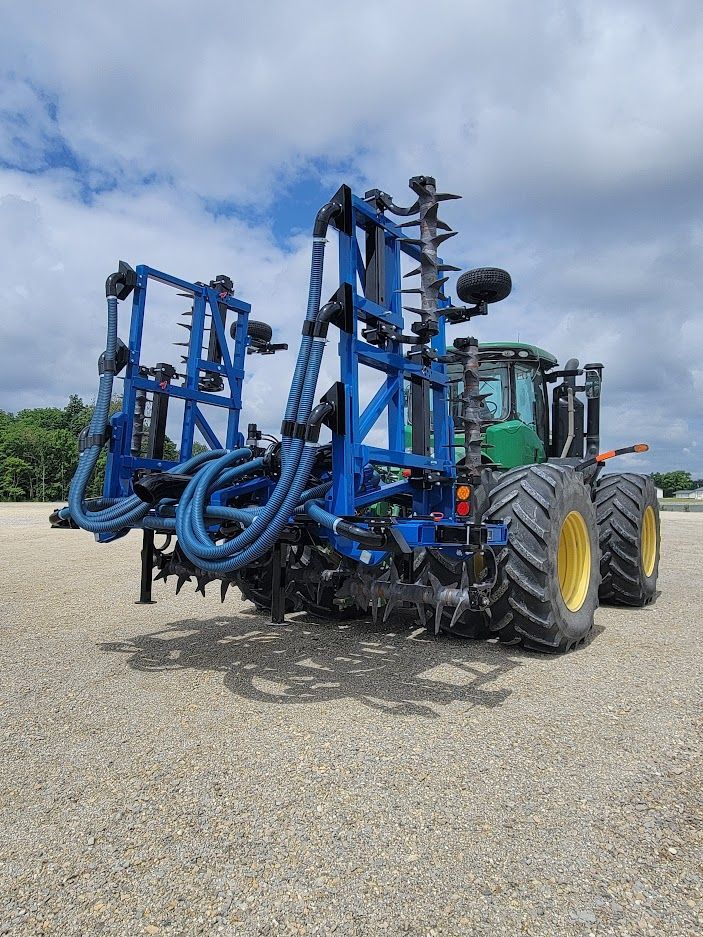 A blue and yellow tractor is parked in a gravel lot.