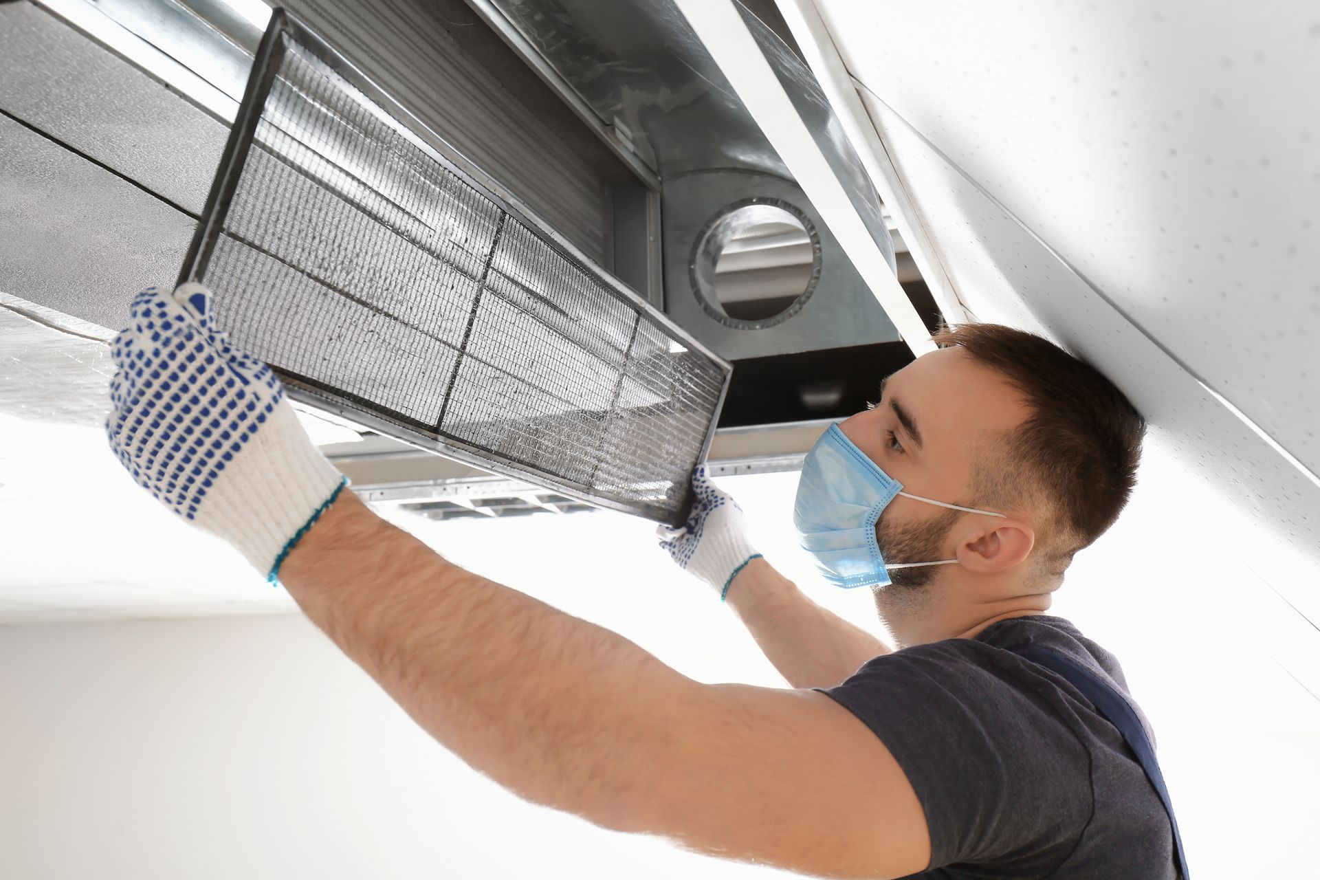 Person wearing gloves and a face mask removing an HVAC air filter.