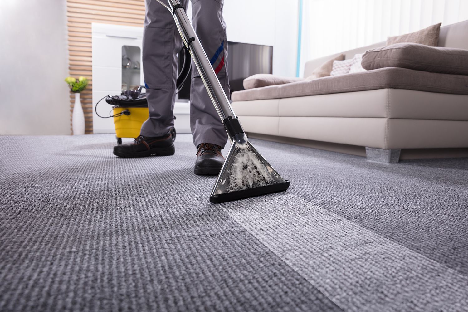 A person uses a vacuum cleaner to clean a carpet, inside a living room.