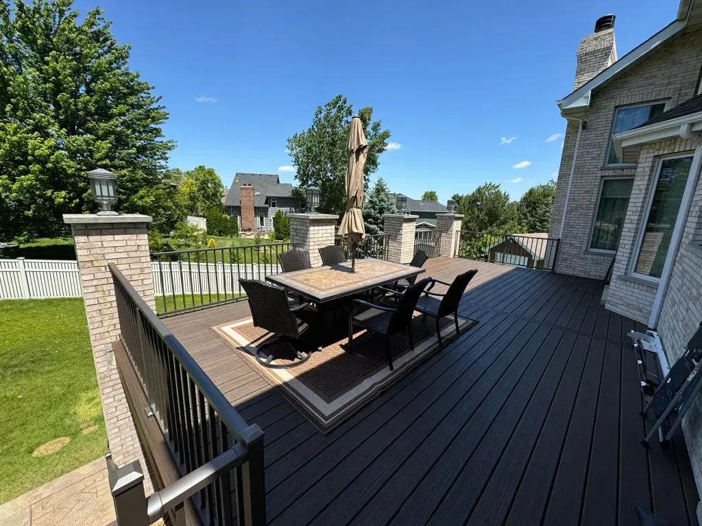 Backyard deck with outdoor dining table, chairs, and clear blue sky beside a stone house
