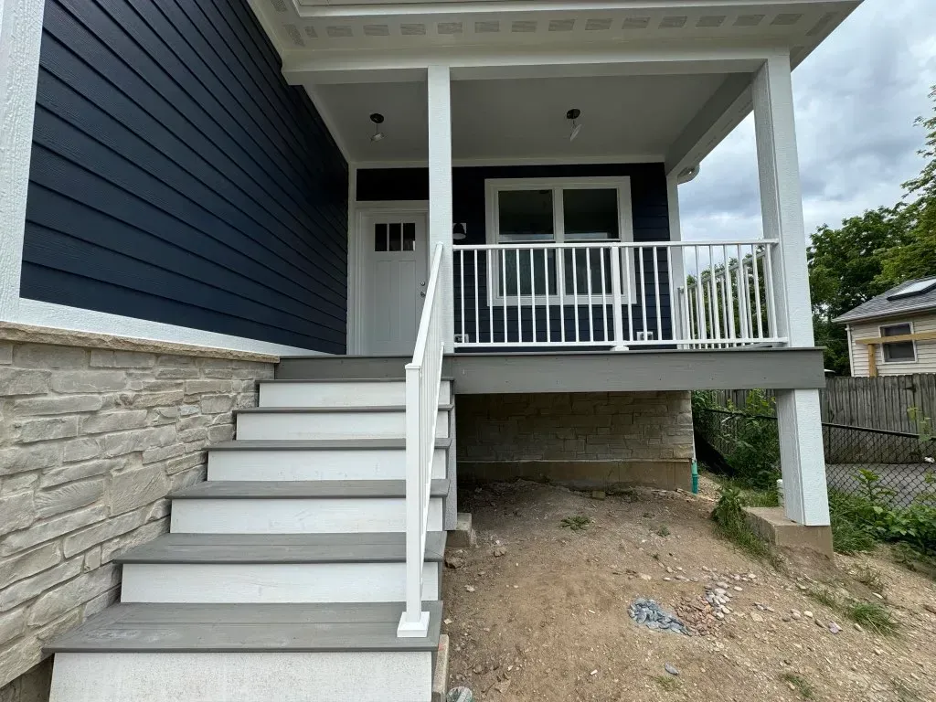 Front porch with white stairs, railing, and covered entry on a blue house with stone foundation.