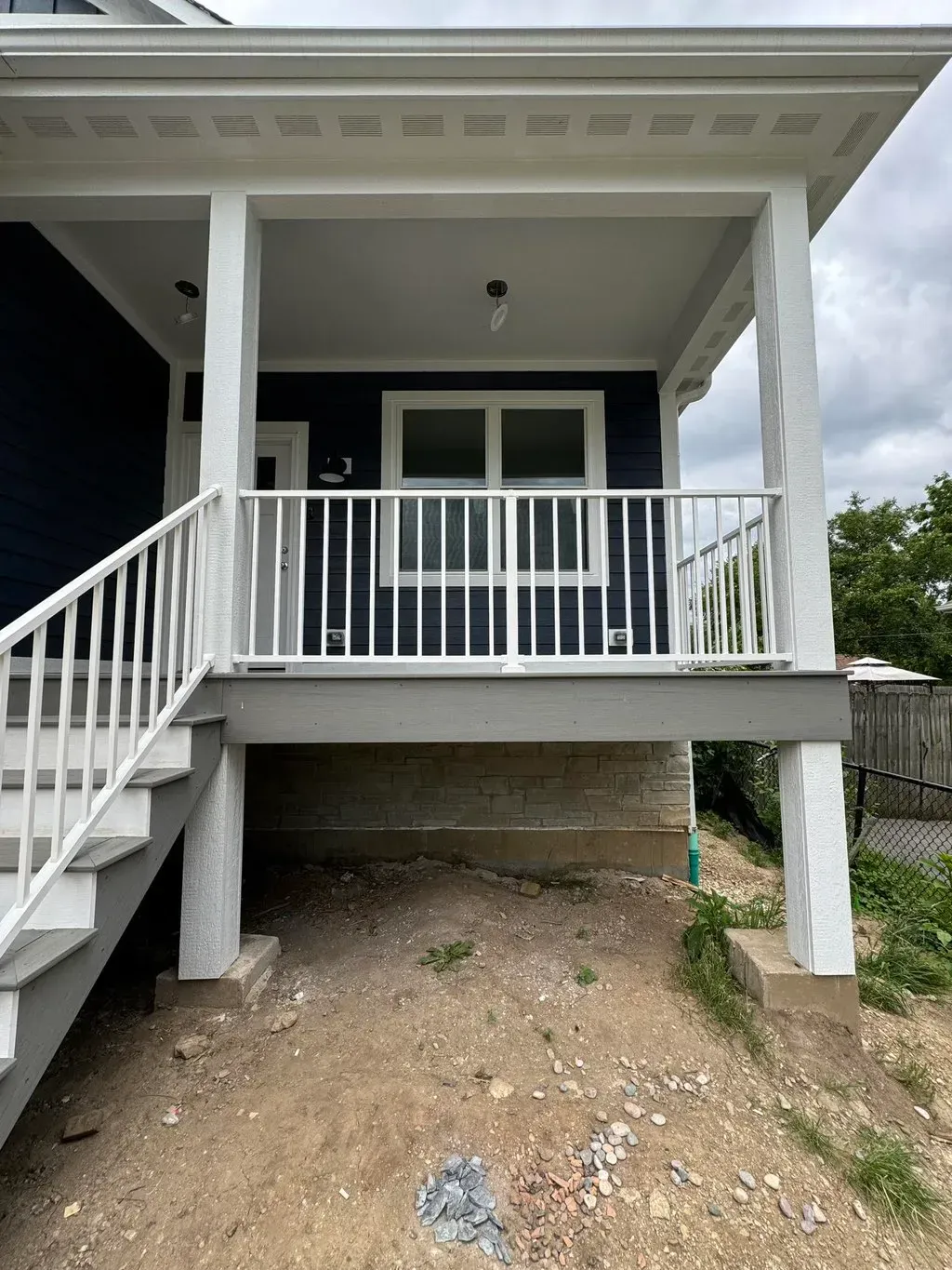 White front porch with stairs, railing, and double doors under a covered roof over a gravel yard.