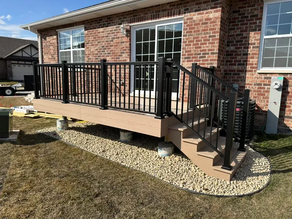 Raised brick patio with black railings and steps beside a house