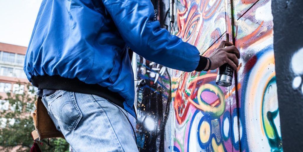 Person in blue jacket spray painting graffiti on a wall.