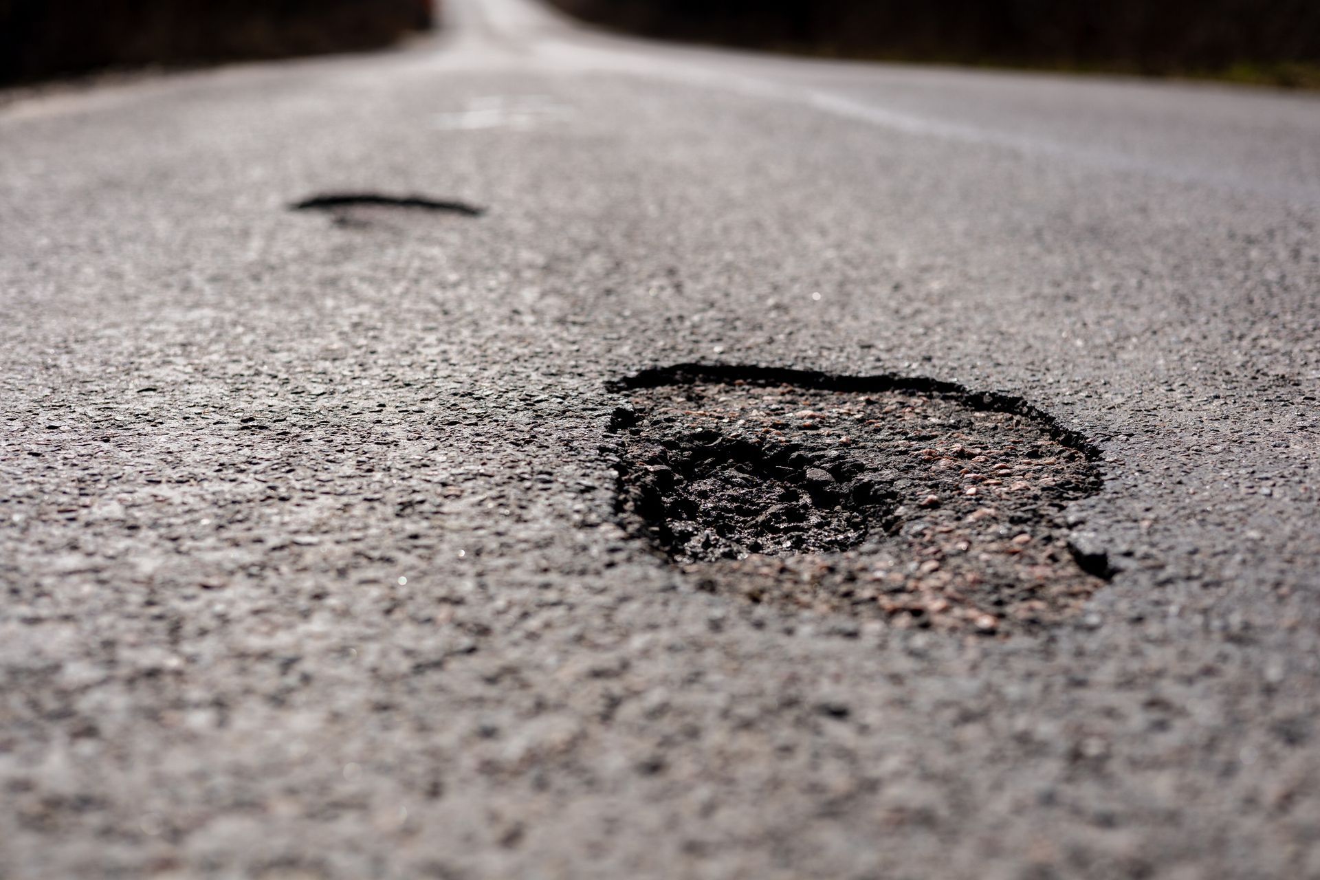 Close-up of asphalt road with potholes, slightly out of focus, blurred background.