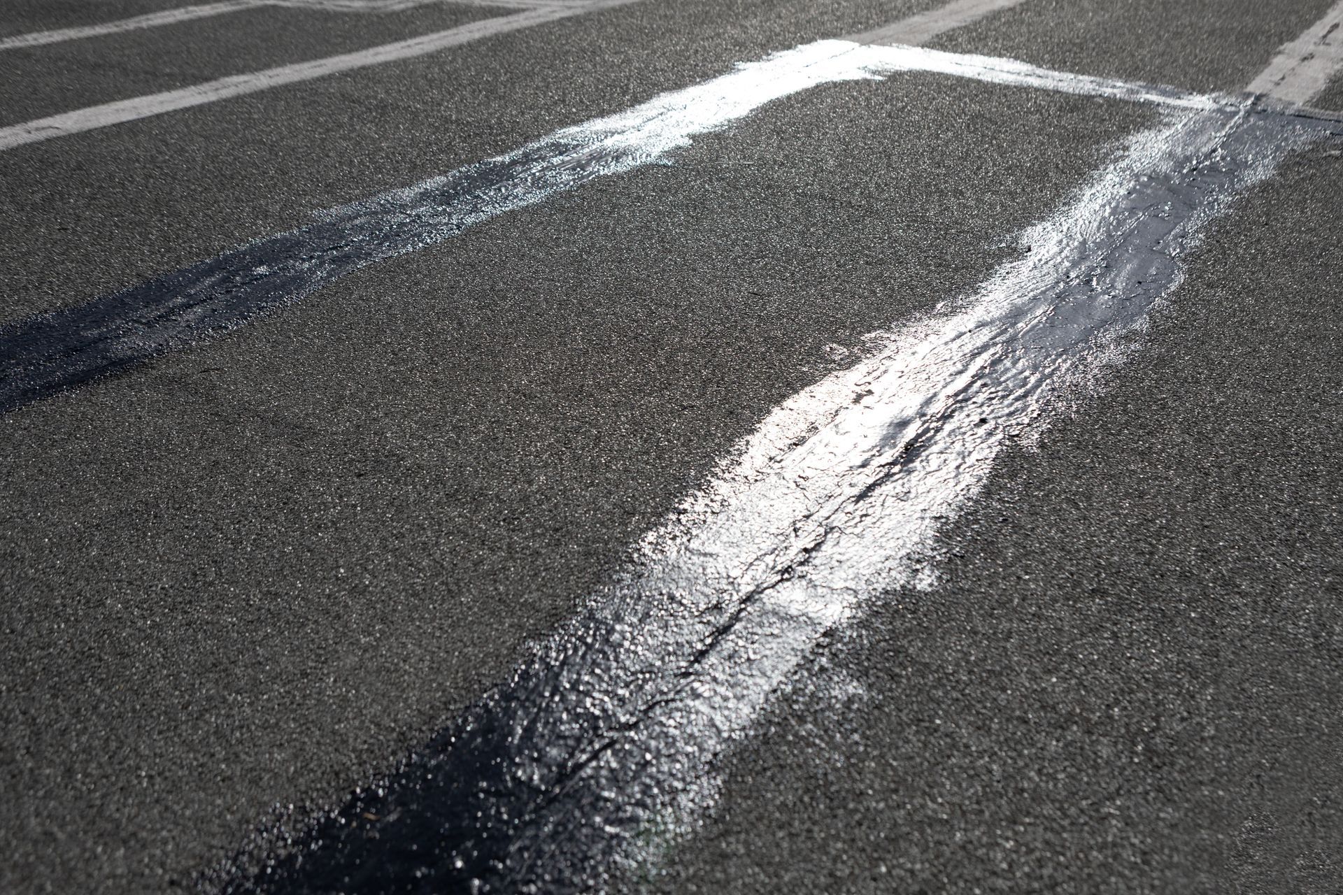 Black sealant applied to cracked asphalt road, forming a rectangle.