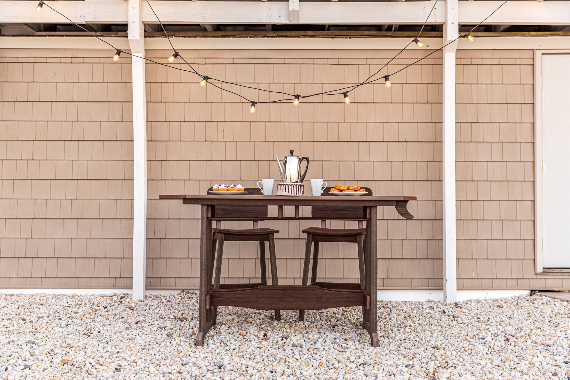 A table with two stools under a canopy with a string of lights hanging from it