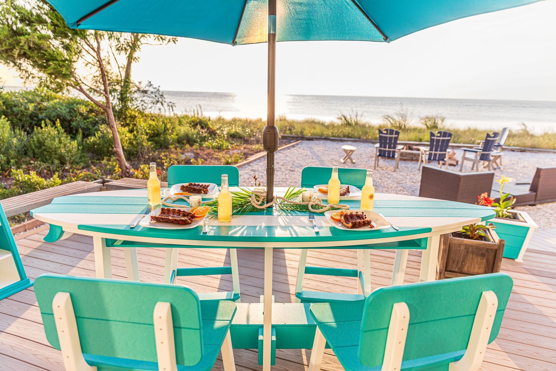A table and chairs under an umbrella on a deck overlooking the ocean.