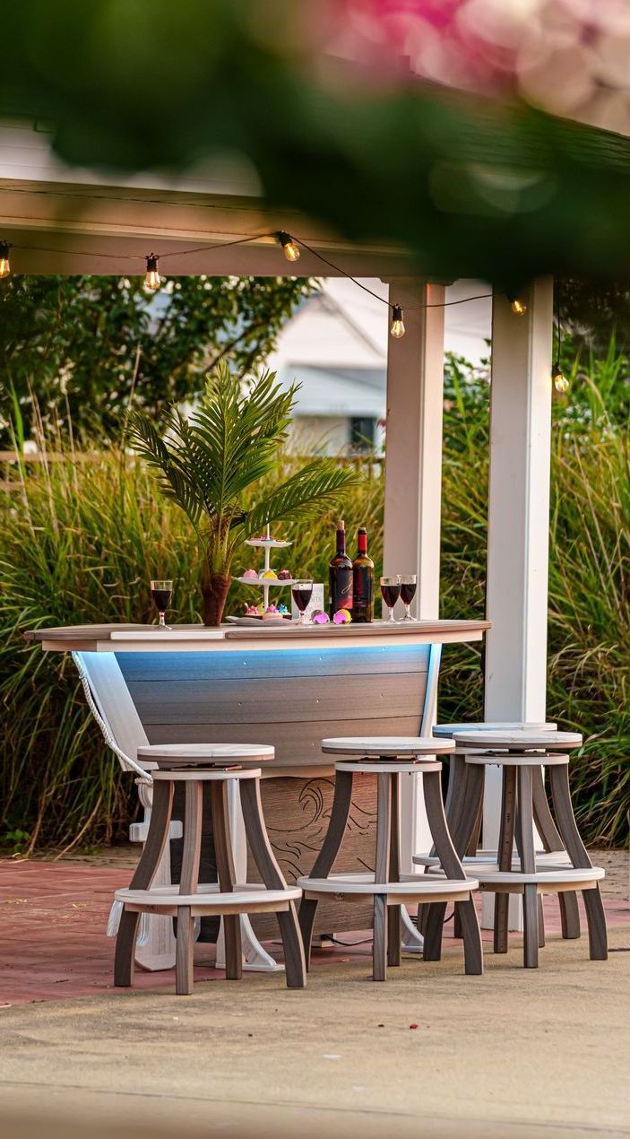 Outdoor bar under a white pergola with stools. The bar features a blue light and is stocked with wine.