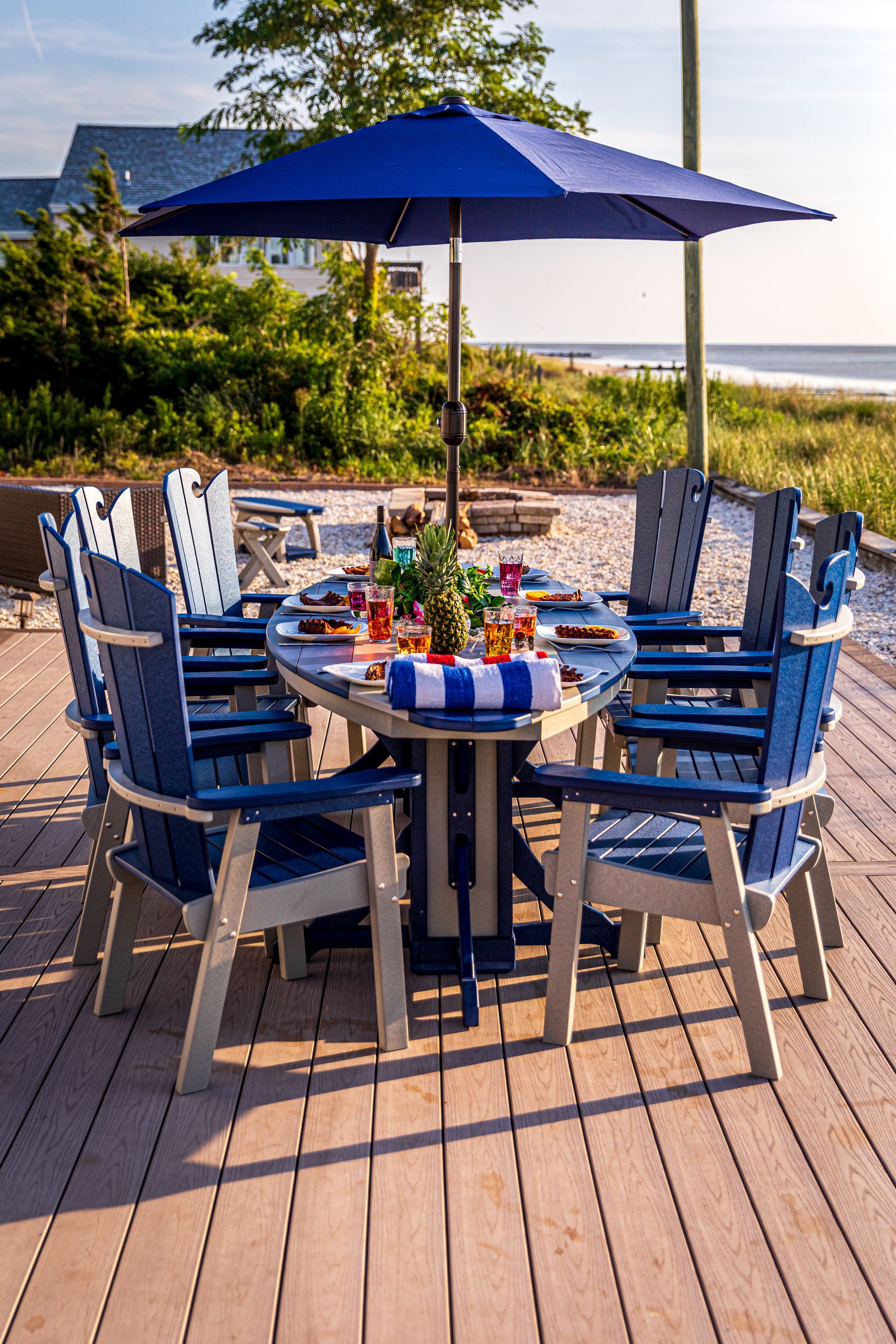 A table and chairs on a deck with a blue umbrella.