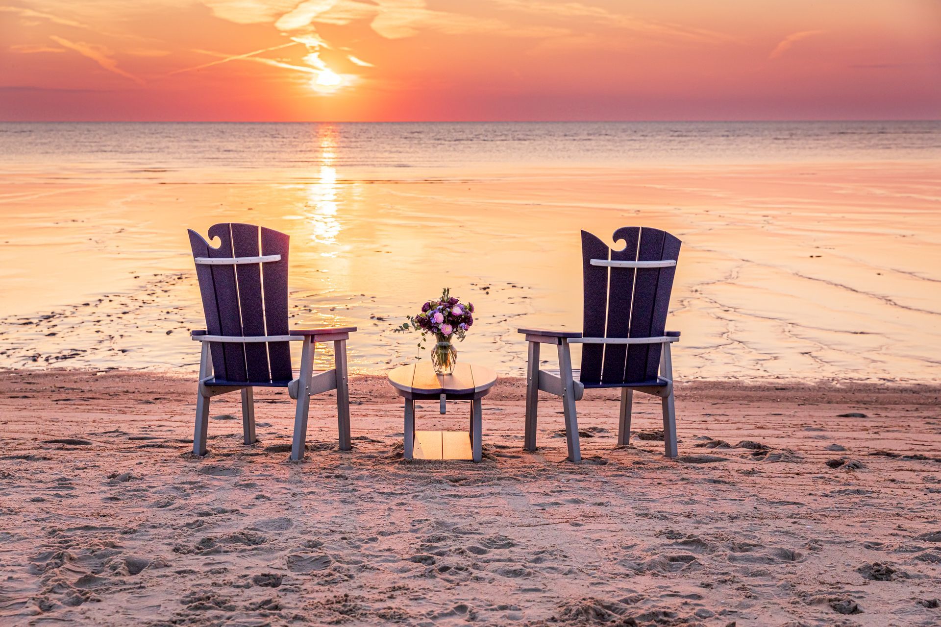 Two chairs and a table on a beach at sunset.