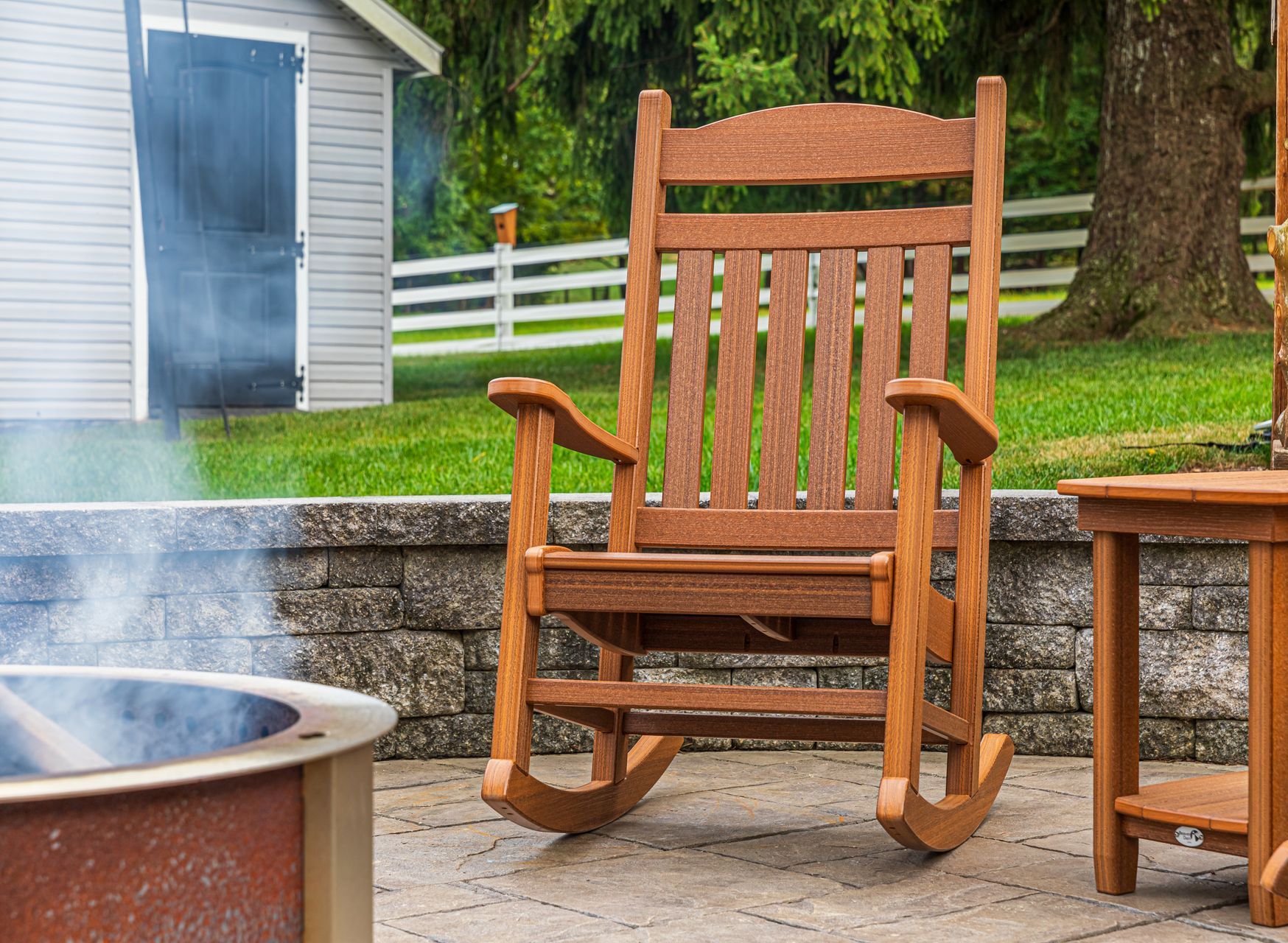 A wooden rocking chair is sitting on a patio next to a fire pit.